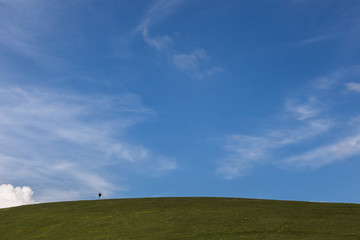 A small human figure on top of a green hill beneath a huge sky