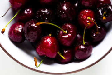 Cherry with water drops in a white-brown bowl on a white background, natural light