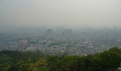 Smog over Seoul City. Skyline of downtown Seoul behind green vegetation with dense man-made smog obstructing the view. View from Namsan television tower, May 2017.