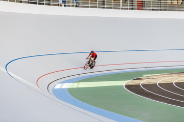 Young professional cyclist on a velodrome. Sports man in a red T-shirt and a black bicycle.