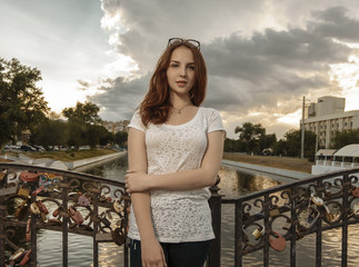 Cute woman on bridge with love locks on fence looking at camera