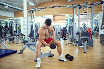 Fototapeta na wymiar Bodybuilder does exercises with dumbbells in the gym.