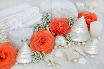 Fototapeta na wymiar Skincare beauty cleansing products with orange rose flowers, soap, moisturising cream, cotton towelling accessories and decorative shells and pearls on distressed white wood background.