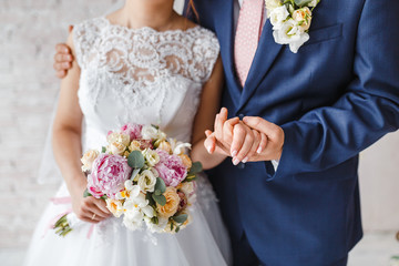 The bride and groom embrace and hold a wedding bouquet of pastel flowers, close-up