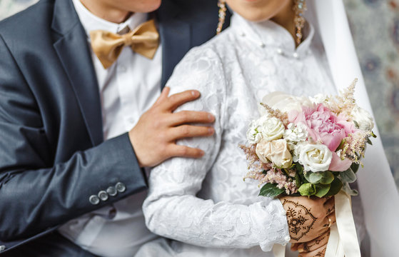 The bride and groom embrace and hold a wedding bouquet of pastel flowers, close-up