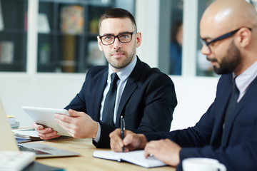 Professional trader with touchpad looking at camera by workplace