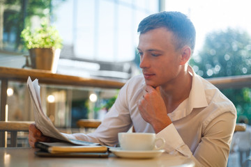Thoughtful man reading a newspaper in a street cafe at lunch.