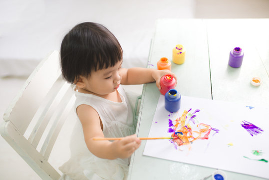 Funny laughing asian baby girl drawing with colorful pencils at home