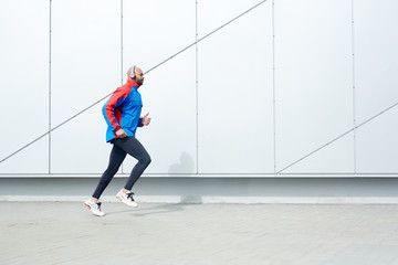 Fototapeta na wymiar Active guy in sportswear running along wall of modern building
