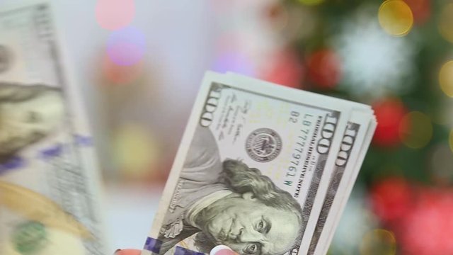 Closeup of female hands holding stack of money in blurry glowing holiday background. Adult woman counting money ready to buy Christmas presents. Real time full hd video footage.