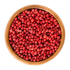 Pink pepper in wooden bowl. Peppercorns, dried berries, spice. Schinus terebinthifolia, Brazilian pepper, aroeira, rose pepper, wilelaiki, Christmasberry. Isolated macro food photo close up over white