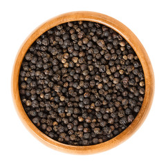 Black pepper in wooden bowl. Dried berries of Piper nigrum are called peppercorns. Made from the unripe drupes of the pepper plant. Spice and seasoning. Isolated macro food photo close up over white.