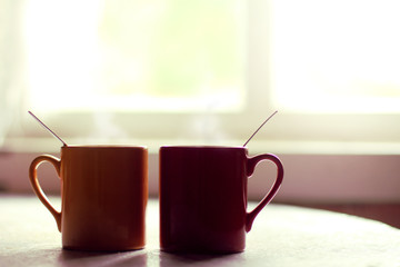 Breakfast together in a cozy atmosphere/ Red and yellow mugs with a hot drink on the table by the window