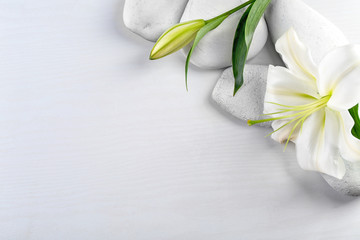 Spa stones and beautiful lily on white wooden background