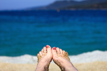 Fototapeta na wymiar Female bare feet from sand on a blurred background of the coast. Woman relaxing on beach by the sea. 