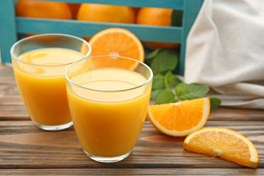 Glasses of tasty orange juice and box with fruit on wooden table