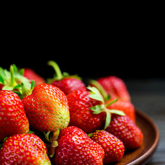 Harvest of fresh organic strawberries on plate isolated on black background macro image