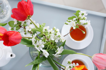 Vase with beautiful flowers and tea set on table at home