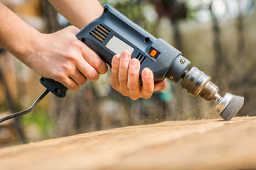 Hands man with electrical rotating brush metal disk sanding a piece of wood