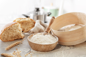 Bowl with flour, sieve and bread chunk on blurred background