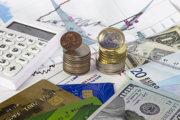 Heap on quarter dollars with one cent on top,heap of euro coins, one euro coin on top. One us dollar bills, hundred dollars bill, euro banknotes. Two credit cards ,ruler and calculator  