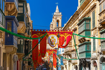 Obraz premium Festively decorated street with banners for St Augustine Feast in the old town of Valletta, Malta. Flaming, arrow pierced heart - symbol of St Augustine