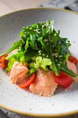 Close-up salad of red fish, arugula, cherry tomatoes, sesame, spices, beautiful trendy dish, restaurant, bright, tasty, colorful