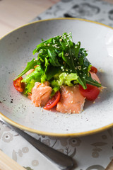 Close-up salad of red fish, arugula, cherry tomatoes, sesame, spices, beautiful trendy dish, restaurant, bright, tasty, colorful