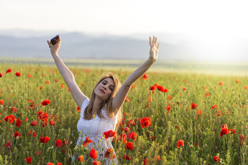 Naklejka na ściany i meble Girl standing in a poppy field with hands up with phone