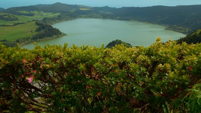 A jib shot revealing the beautiful Lagoa das Furnas lake from behind scenic vegetation, in the island of Sao Miguel, The Azores, Portugal. The Azores are one of the hidden gem destinations in Europe.