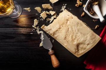 Gordijnen Slice of parmesan cheese with knife, nuts and wine over a wooden table © Javier Somoza
