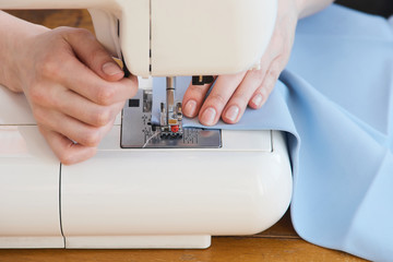 Seamstress threading blue textile on sewing machine close up
