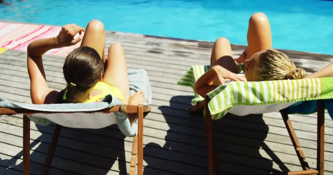 Two womens interacting with each other while sunbathing near swimming pool