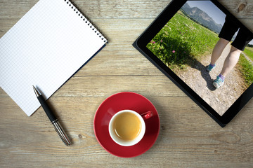 Tablet mit Beine einer Frau bei einer Wanderung in den Bergen mit Wiese