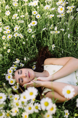 Beautiful woman enjoying daisy field, nice female lying down in meadow of flowers, pretty girl relaxing outdoor, having fun, holding plant, happy young lady and spring green nature, harmony concept