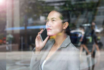 business woman using a smartphone at reflection glass of office building.