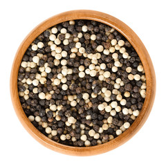 Black and white pepper in wooden bowl. Also called Mignonette pepper. Peppercorns, dried berries of Piper nigrum. Spice and seasoning. Isolated macro food photo close up on white background.