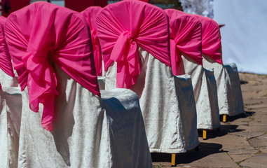 Chairs for guests on wedding ceremony with white and pink satin cloth outdoor