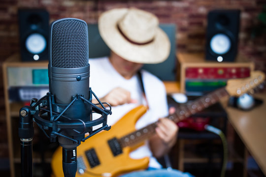 condenser microphone on male musician playing electric guitar in music studio background