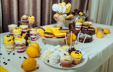 Holiday candy bar in yellow and brown color. Wedding candy bar served with cupcakes, cake pops, desserts in glasses, lemons and coffee beans