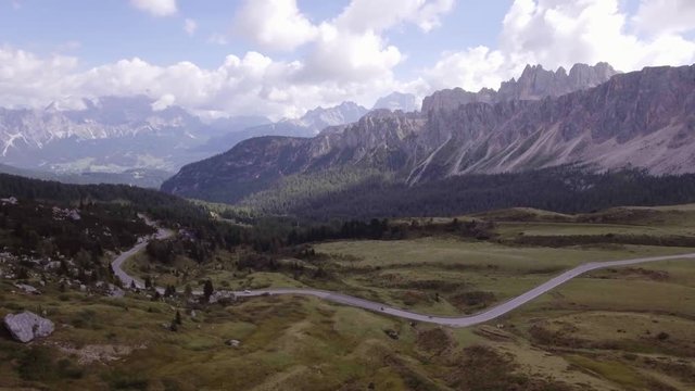 Aerial drone flight establisher over road and green forest.Summer adventure journey in mountain nature outdoors. Travel exploring Alps, Dolomites, Italy. 4k video side