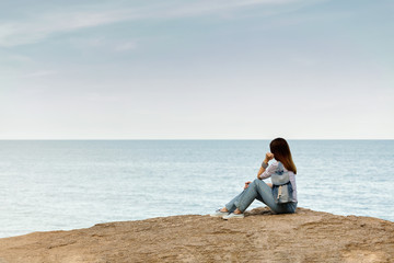 Young woman in jeans, in striped top and sneakers on the beach by the sea.
