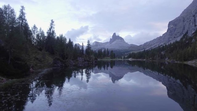 Aerial drone flight establisher over lake with evening clouds and forest.Summer adventure journey in mountain nature outdoors. Travel exploring Alps, Dolomites, Braies, Italy. 4k video side