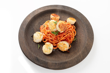 Pasta with fried scallops, oregano and tomato sauce on black wooden plate