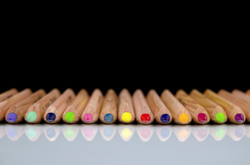 Close-up view of colored pencils lying on glossy white background with reflection isolated on black background © Forgem