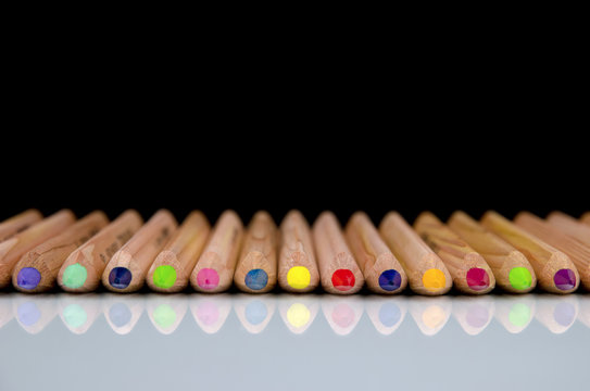 Close-up view of colored pencils lying on glossy white background with reflection isolated on black background