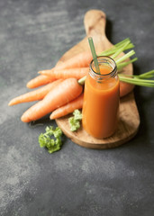 A bottle of fresh carrot juice with fresh carrots on dark background.