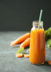 A bottle of fresh carrot juice with fresh carrots on dark background.