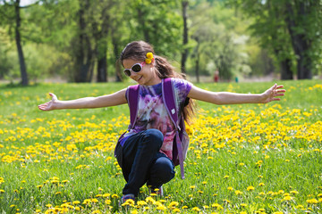 A girl in sunglasses is sitting on the meadow with her arms outstretched.