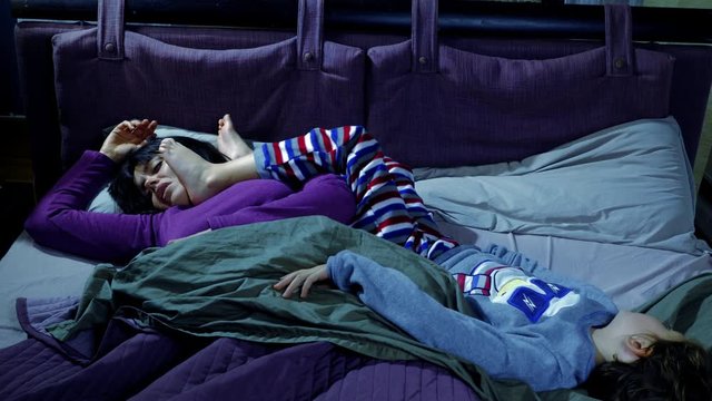 Woman at night sleeping with feet of son in face in bed funny